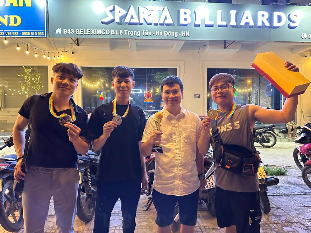 Bốn thành viên đứng trước quán bi-a, khoe huy chương và cúp