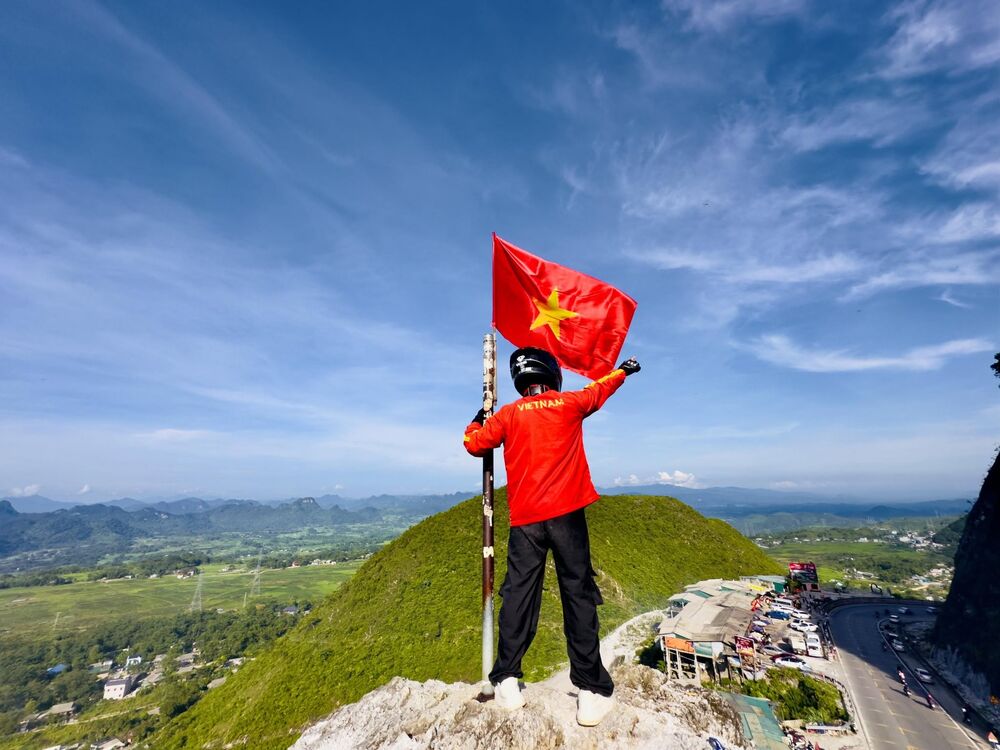 Một thành viên cầm cờ Tổ quốc đứng trên mỏm đá nhìn xuống thung lũng